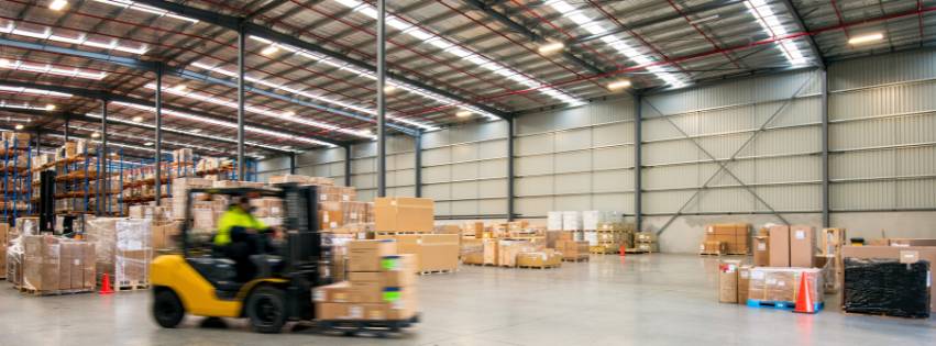 Warehouse full of boxes and a forklift driving by.