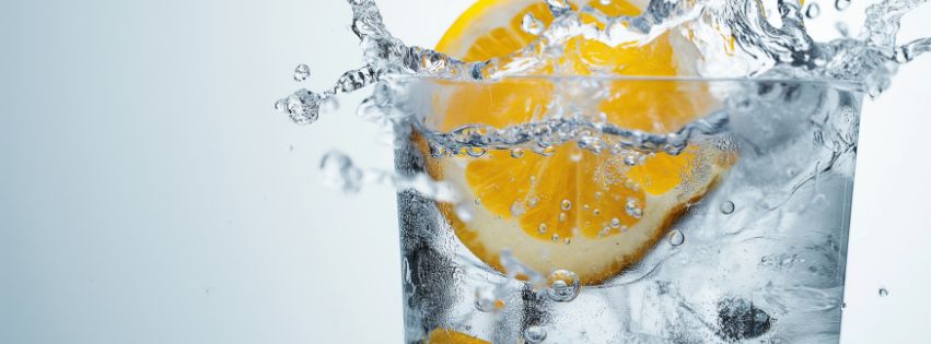 Lemon slice being dropped into a glass of water.