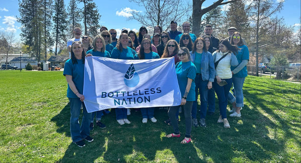 Group of people holding a 'Bottleless Nation' banner outdoors on a grassy area.
